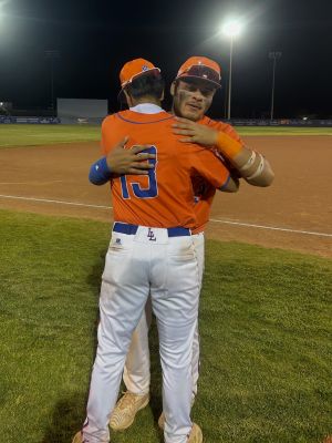 Eric Pedro Jr. in Los Lunas jersey 13 embracing a teammate after a night baseball game