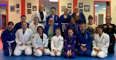 Women and girls in gi posing together on the mats at Eric Pedro BJJ